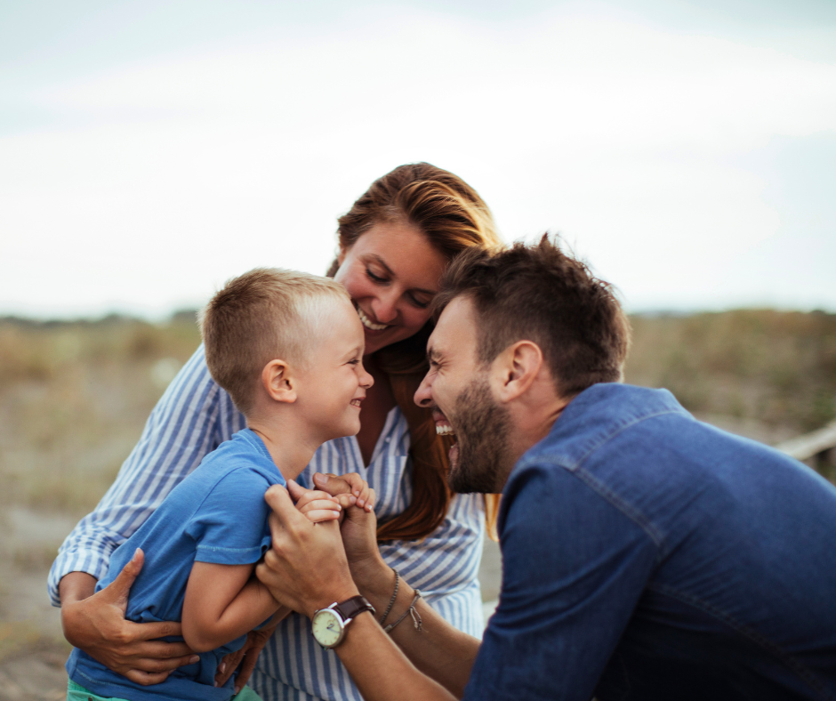 Smiling parents happily playing with their young son outdoors on a sunny day.