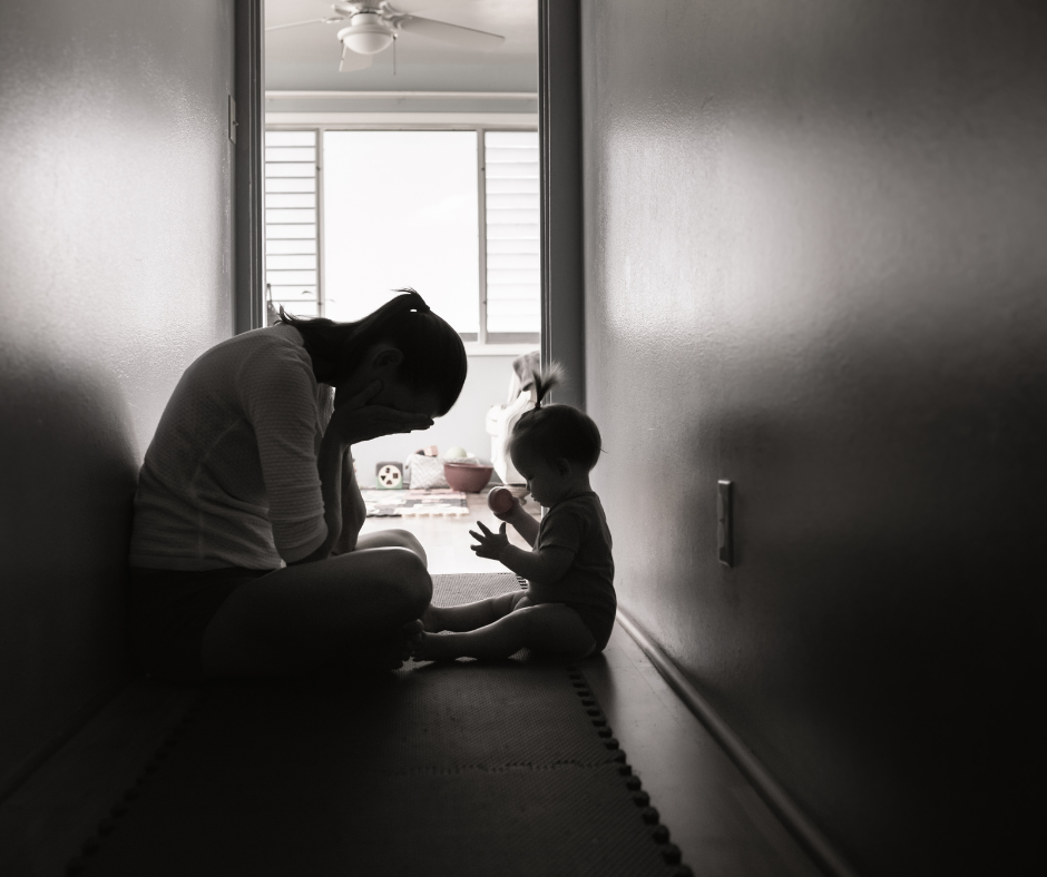 A mother sitting in a dimly lit hallway with her baby, symbolizing challenges of parenting with depression or anxiety during custody battles.