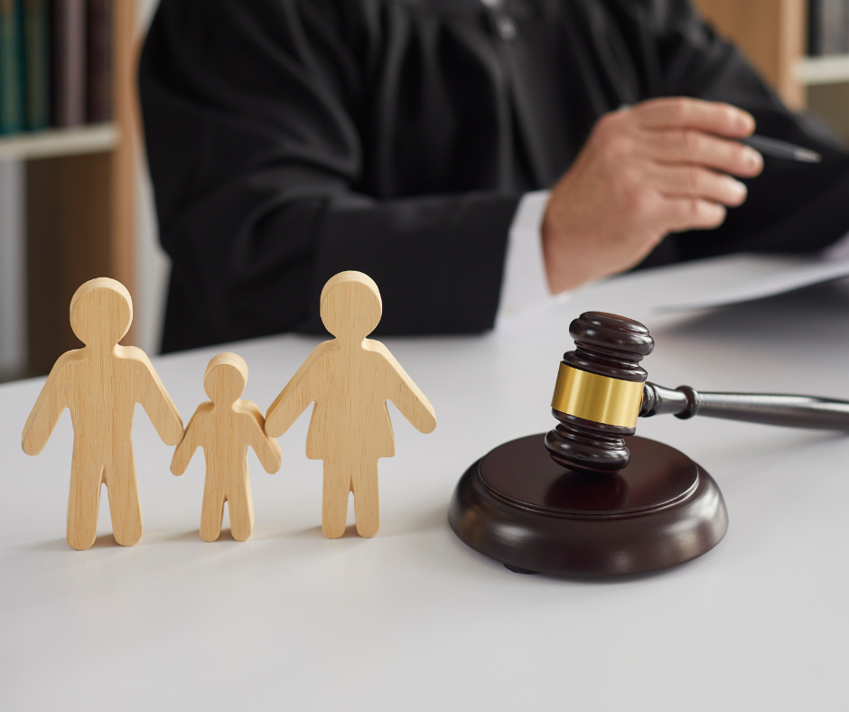 Wooden figures of a family in front of a judge with a gavel on a table, symbolizing custody and legal proceedings.