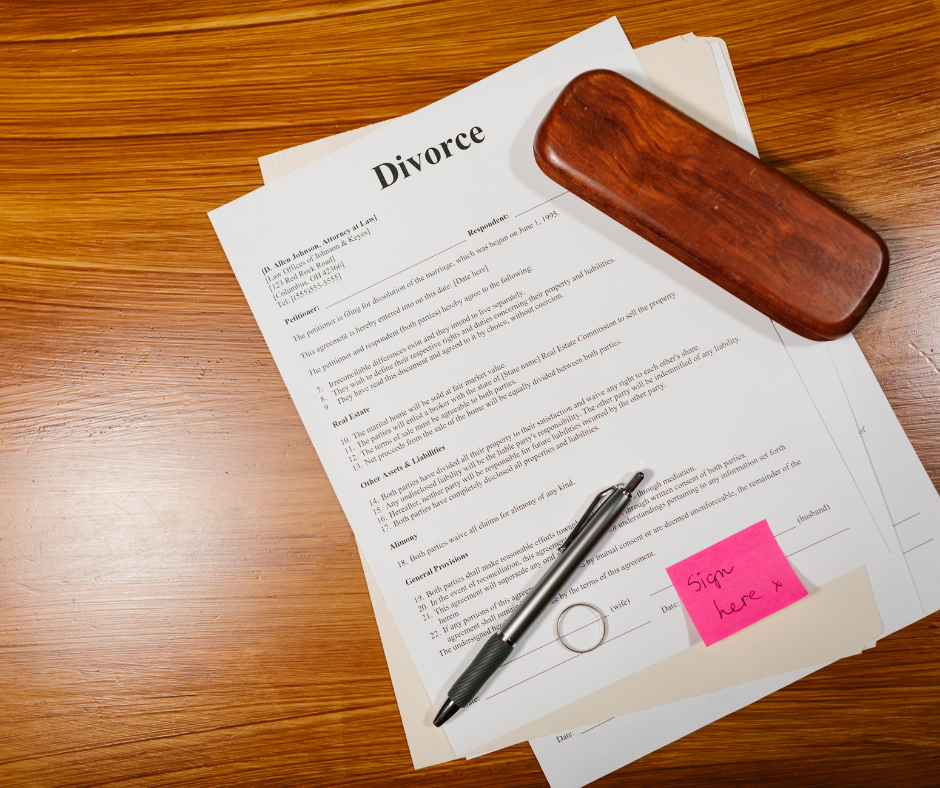 Divorce paperwork with pen, wedding ring, and “sign here” note on a wooden desk, symbolizing the divorce process